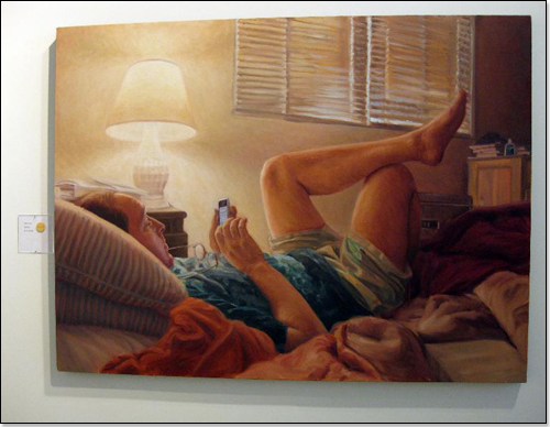 Person relaxing on bed, viewing cell phone, illuminated by lamp.