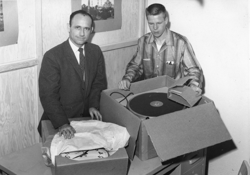 Bob Ballou, the first station manager of KFJC, opens boxes of new equipment, including the turntable and wall clock with George Castleberry. Photo from April 3, 1959 edition of Foothill Sentinel. 