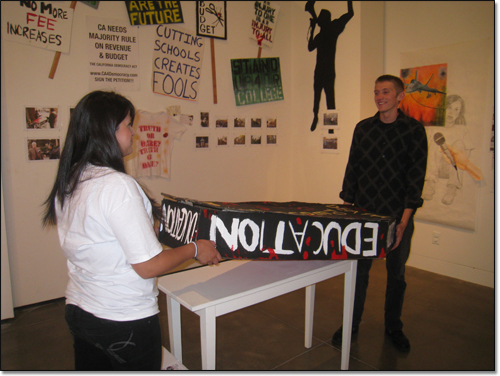 Two activist students installing a coffin-like sculpture with 'Education' written on it.