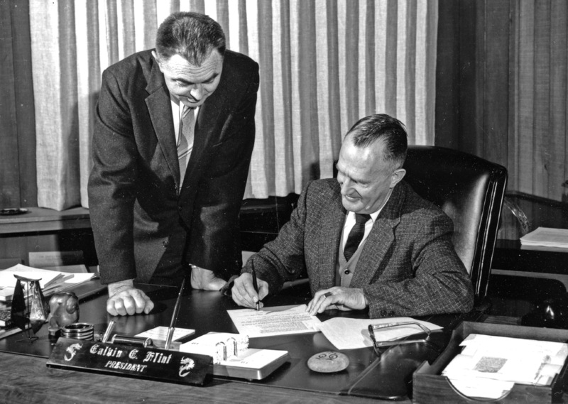 Earl Goddard, Chairman of the board of the Perham Foundation, looks on as Dr. Calvin C. Flint, president of Foothill College, signs an agreement paving the way for a fund drive by the Foundation to finance an electronics museum on the Foothill College Campus. Photo taken in 1960s; precise date unknown. 