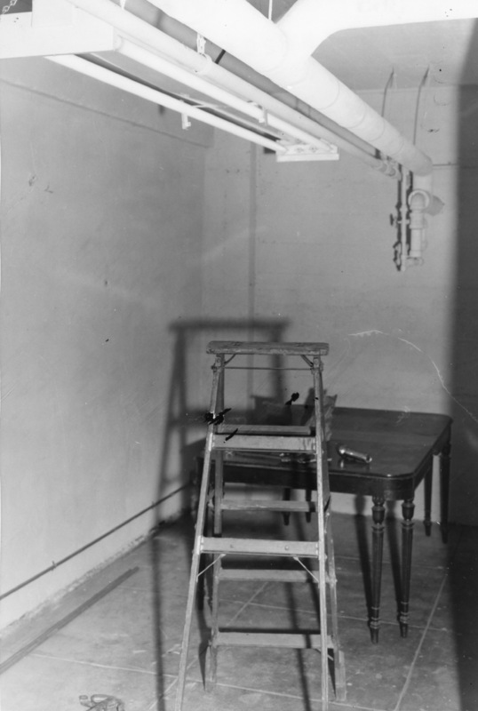 Construction of KFJC radio studio in basement of Foothill College, 1959. Photo of ladder, table and flashlight with overhead pipes and fluorescent lights. 