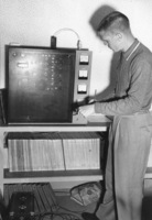 Bob Ballou, station manager, examines radio equipment in the basement of Foothill College in Mountain View in this photo from 1959. Records and daily binders visible on lower shelves. 