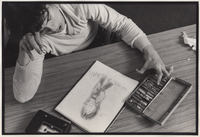 Artist at desk with drawing and art materials.