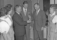 Dr. Calvin C. Flint, holding the match, lights an owl shaped candle to open the Candle Show fundraiser sponsored by the Women's Auxiliary of El Camino Hospital in Mountain View.  Dr. Clark Snead (holding candle)  and Ed Hawkins of El Camino Hospital stand next to him. The nurses are not identified. Picture taken at El Camino Hospital in early 1960s. 