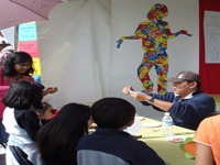 Male college student demonstrating art  to students around an art table.