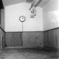 Construction of KFJC radio studio in basement of Foothill College, 1959. Photo of unfinished studio with clock on wall and overhead pipes. 
