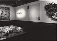 Gallery installation including sculpture and a large feathered cape on one wall.