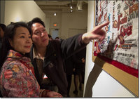 Two museum visitors , one pointing at a detail of Flo Oy Wong's art.