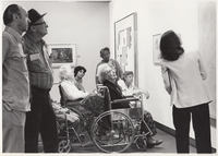 Docent gives exhibition tour to seniors, several using wheelchairs.