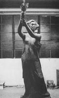 Photo of sculpture of woman holding torch. Background is empty warehouse.