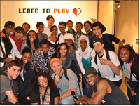 Group photo of First Thursday performers in front of Learn to Play wall sign with its half white, half red heart logo.