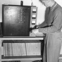Bob Ballou, station manager, examines radio equipment in the basement of Foothill College in Mountain View in this photo from 1959. Records and daily binders visible on lower shelves. 