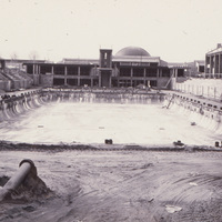 The two swimming pools at De Anza are almost complete. A concrete tower for diving can be seen at the far end of the pool and, just behind the diving tower is the planetarium dome. 