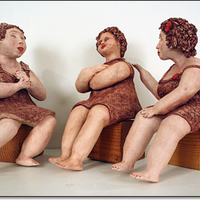 Sculpture of three women casually sitting on boxes, bare feet, talking animatedly.