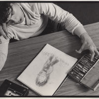Artist at desk with drawing and art materials.