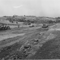 Heavy equipment rolls over rough spots in the dirt road in preparation for the construction of Foothill College. 