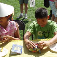 Two students creating art at a table in a sunny outdoor setting. 