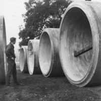 An unidentified man examines the huge concrete sewer lines before they are lowered into place.