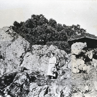Mrs. Willard M. Griffin stands on the large rocks that now highlight the main entrance to the Foothill College Campus. Behind Mrs. Griffin is a pagoda style structure. The Griffins became enamored of Japanese culture and architecture and used this style of structure on many areas of their land.