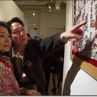 Two museum visitors , one pointing at a detail of Flo Oy Wong's art.