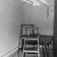 Construction of KFJC radio studio in basement of Foothill College, 1959. Photo of ladder, table and flashlight with overhead pipes and fluorescent lights.