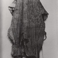 Print of child standing alone and blanket covering all but sock-covered feet.
