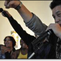 Performers close up, microphone, some with outstretched arms.