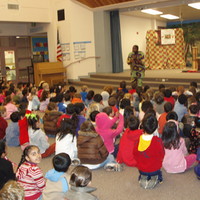 School assembly from a distance. Students watch artist on low stage.