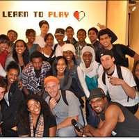 Group photo of First Thursday performers in front of Learn to Play wall sign with its half white, half red heart logo.